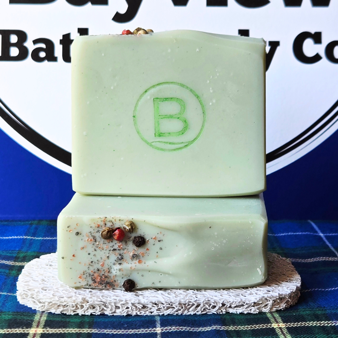 Two green soap bars with visible ingredients on a white lace doily against a blue plaid background with 'Bayview Bath & Body Co' branding.