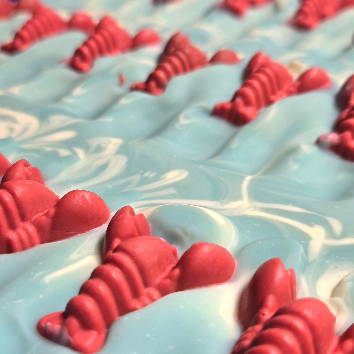 Small red lobsters made of soap on a light blue and white marbled background